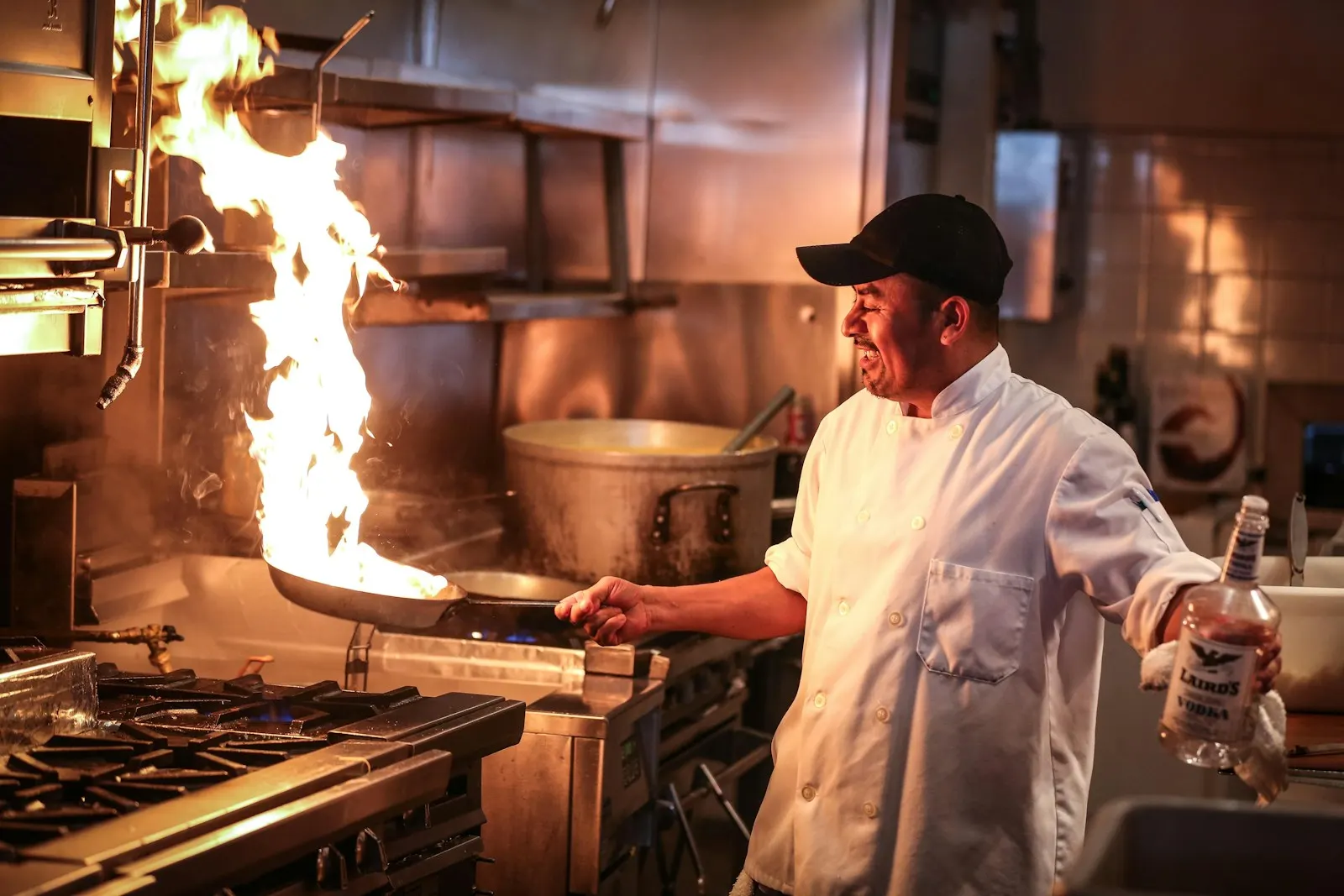 A chef cooking over a flaming pan in a busy kitchen